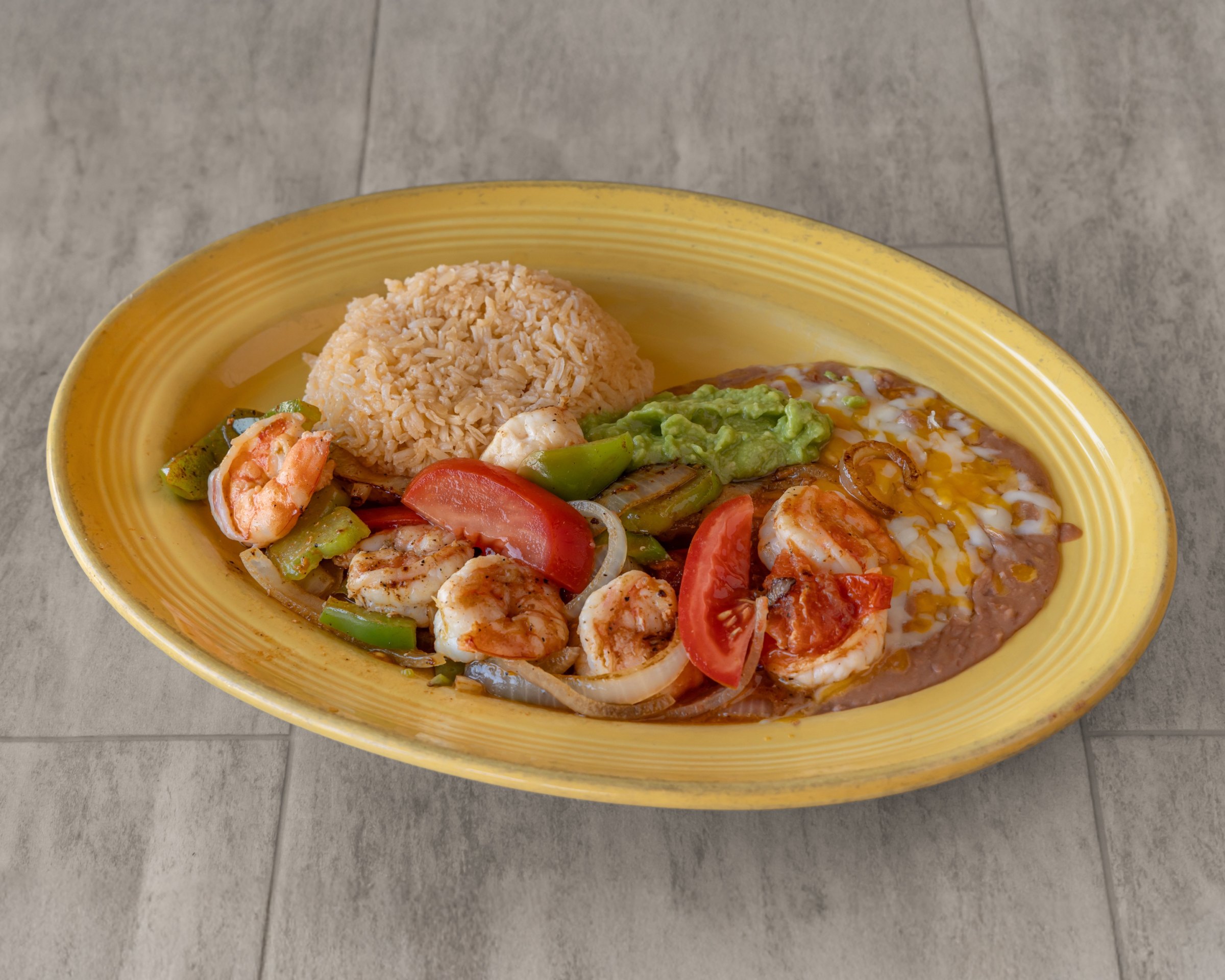 Grilled shrimp with peppers, onion and tomato, rice, guacamole and refried beans with cheese on a yellow plate