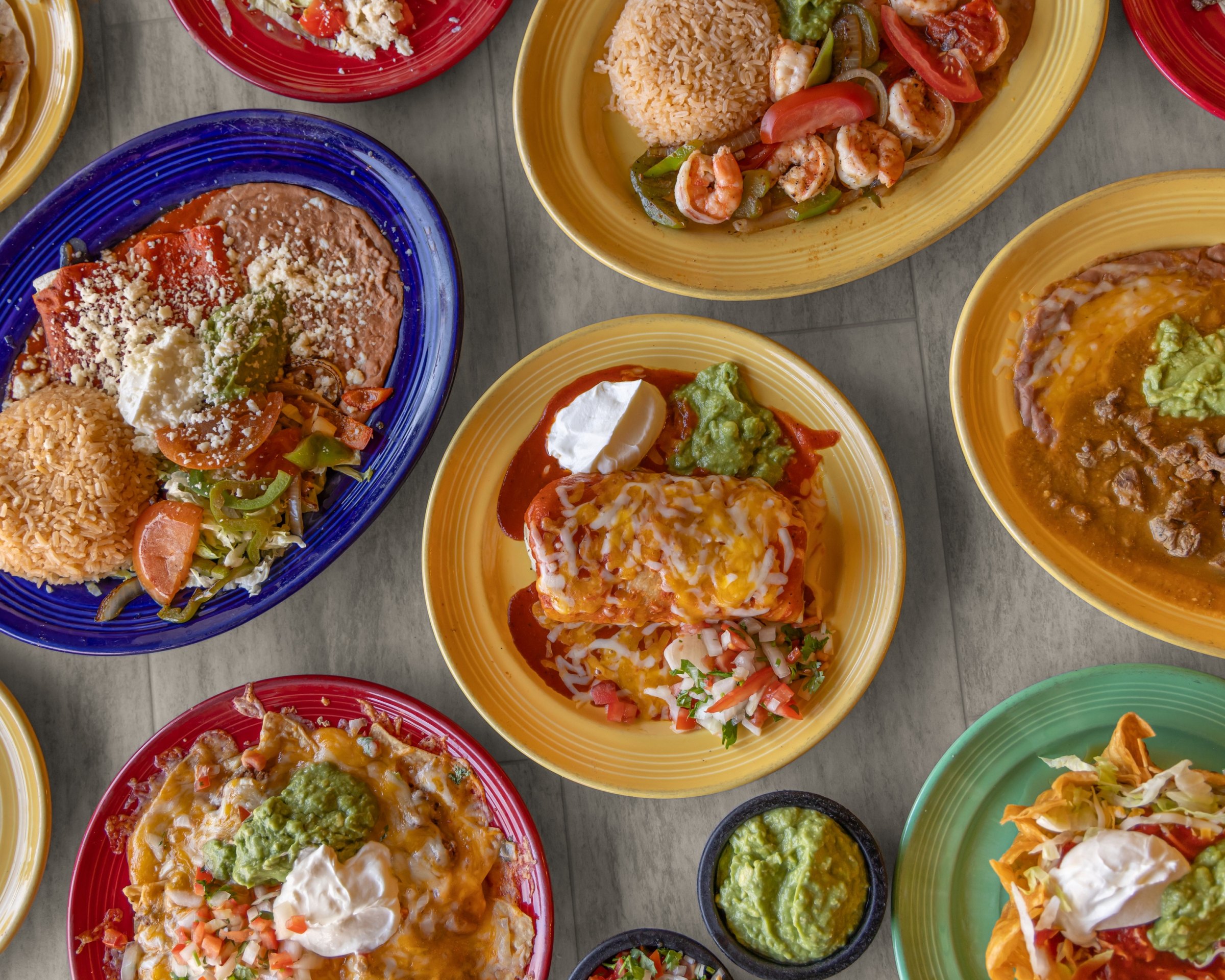 Overhead view of several Mexican dishes on colorful plates, with guacamole in a small bowl