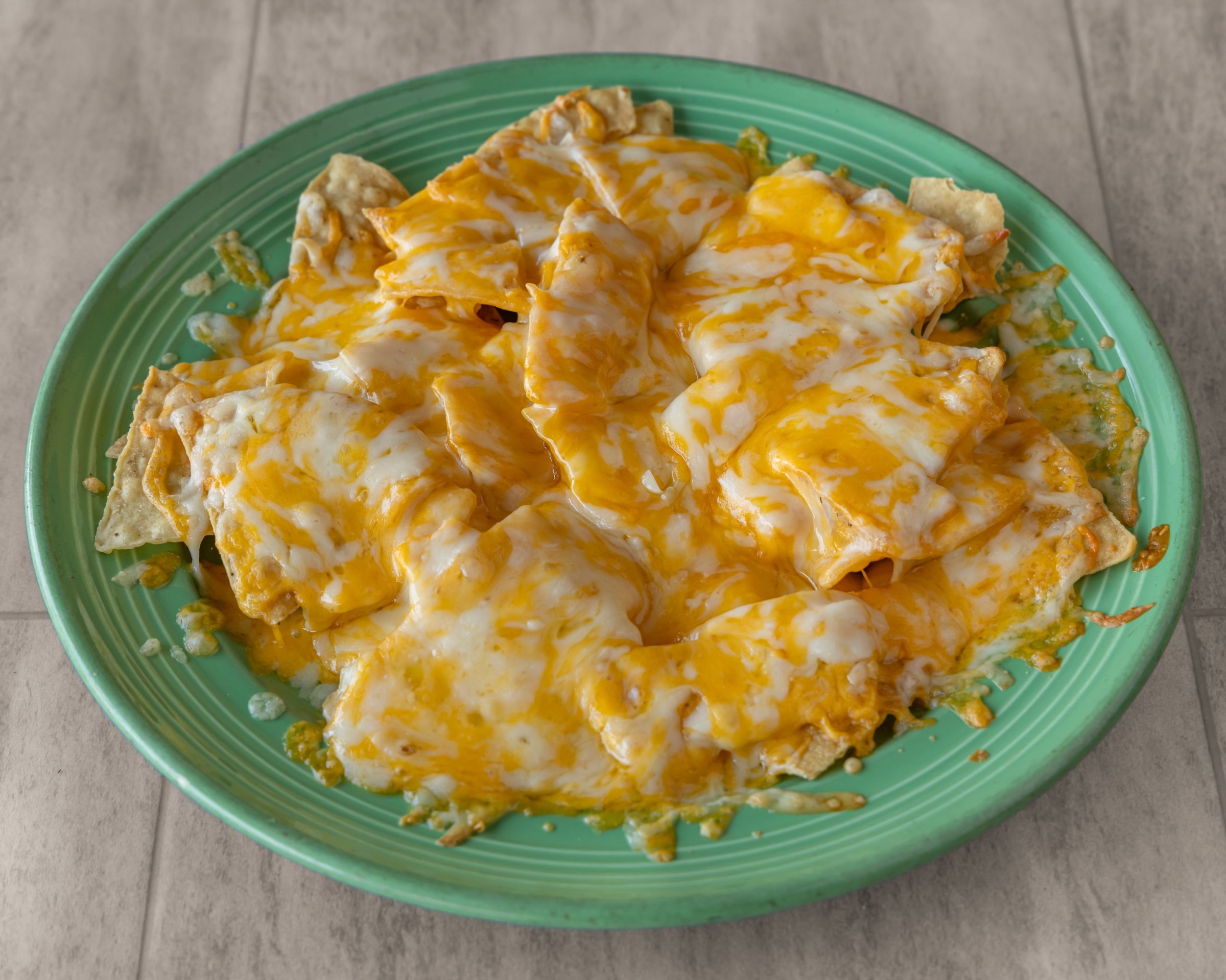 Nachos covered in melted cheese on a green plate