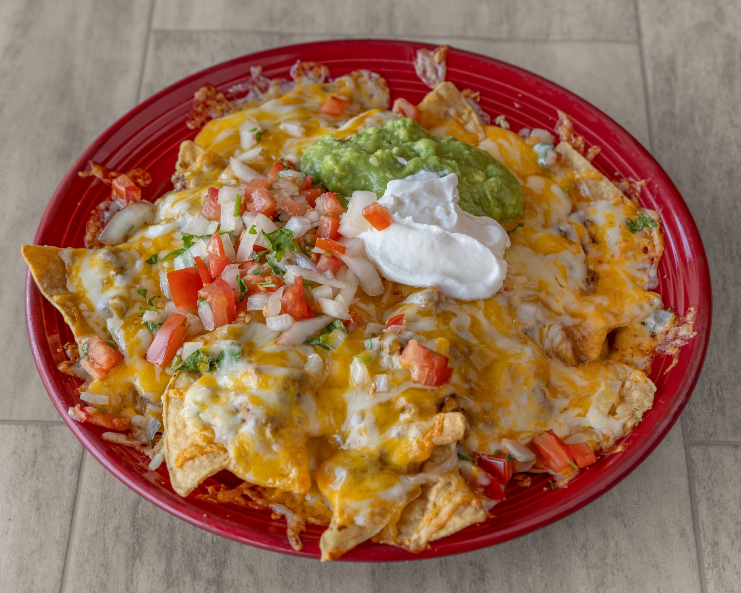 Nachos with melted cheese, pico de gallo, guacamole and sour cream on a red plate