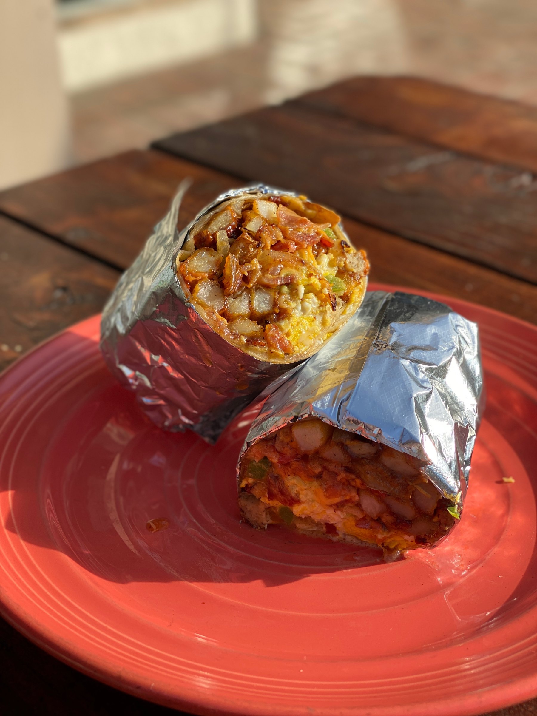 A California breakfast burrito cut in half, wrapped in foil, on a red plate