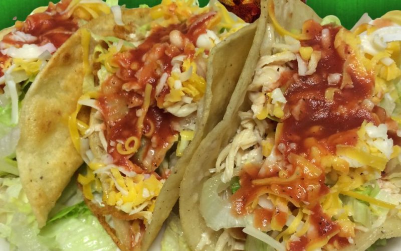 Three crunchy tacos with lettuce, cheese and red sauce