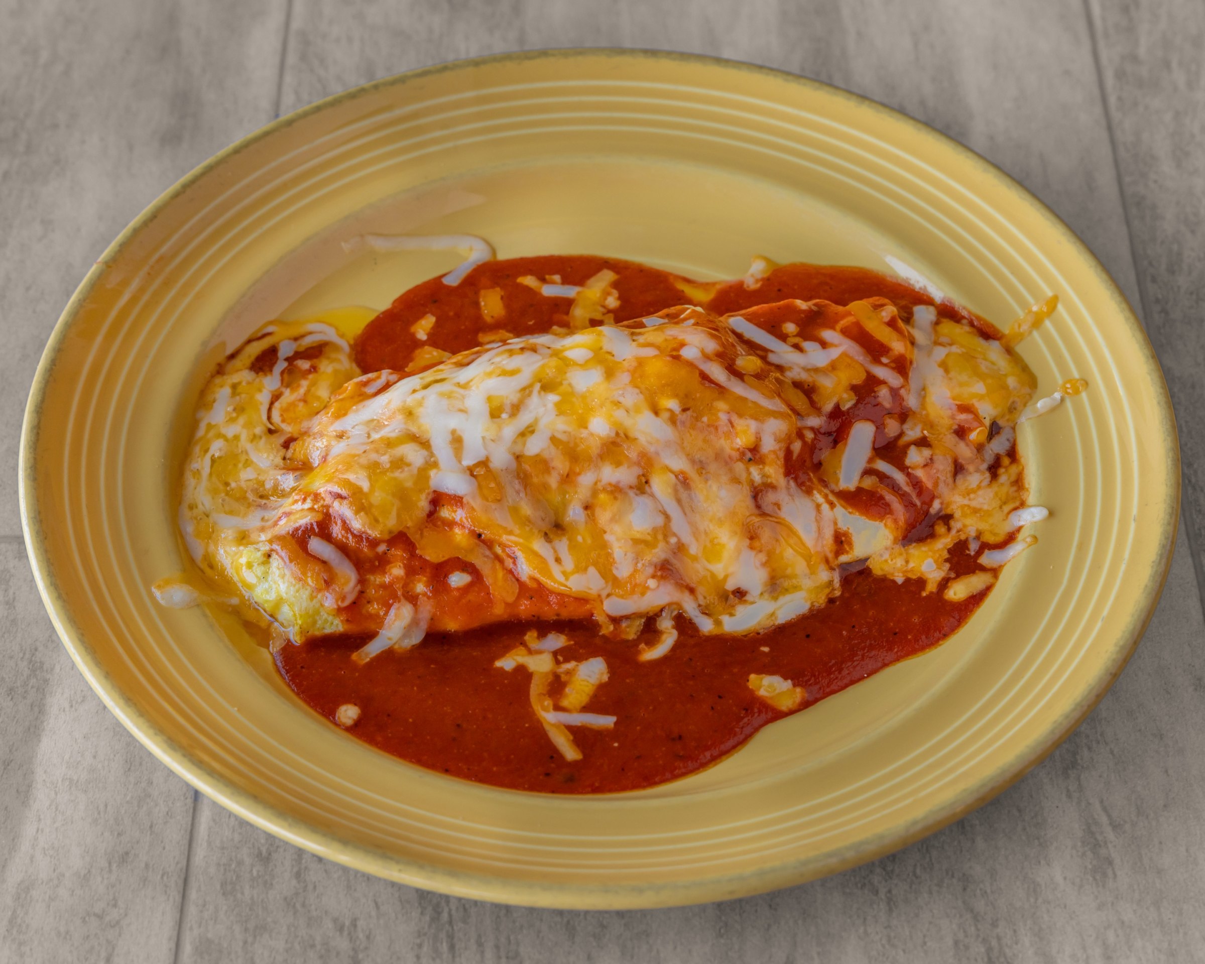 A burrito topped with red sauce and melted cheese on a yellow plate